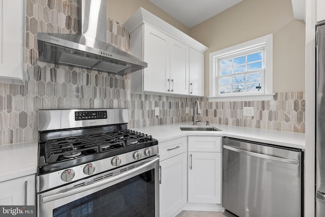 kitchen featuring stainless steel appliances, light countertops, white cabinets, a sink, and wall chimney range hood