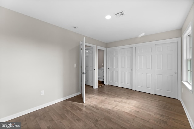 unfurnished bedroom with baseboards, visible vents, dark wood finished floors, and two closets