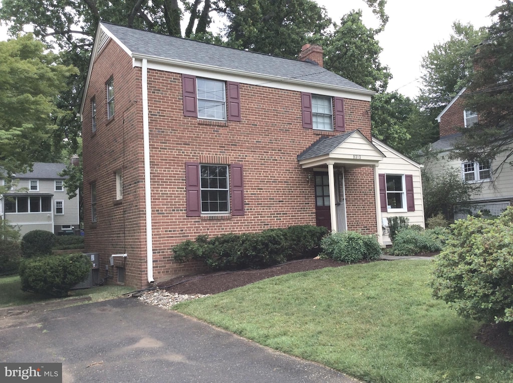 view of front of house featuring a front yard, a chimney, and brick siding