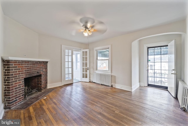 unfurnished living room with radiator, wood-type flooring, a fireplace, and baseboards