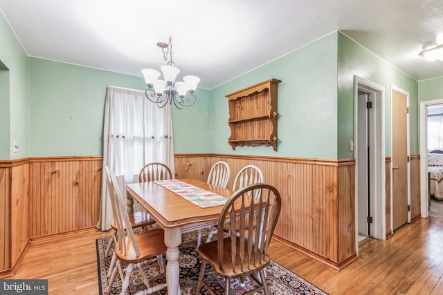 dining room featuring wooden walls, a wainscoted wall, a notable chandelier, and light wood-style flooring