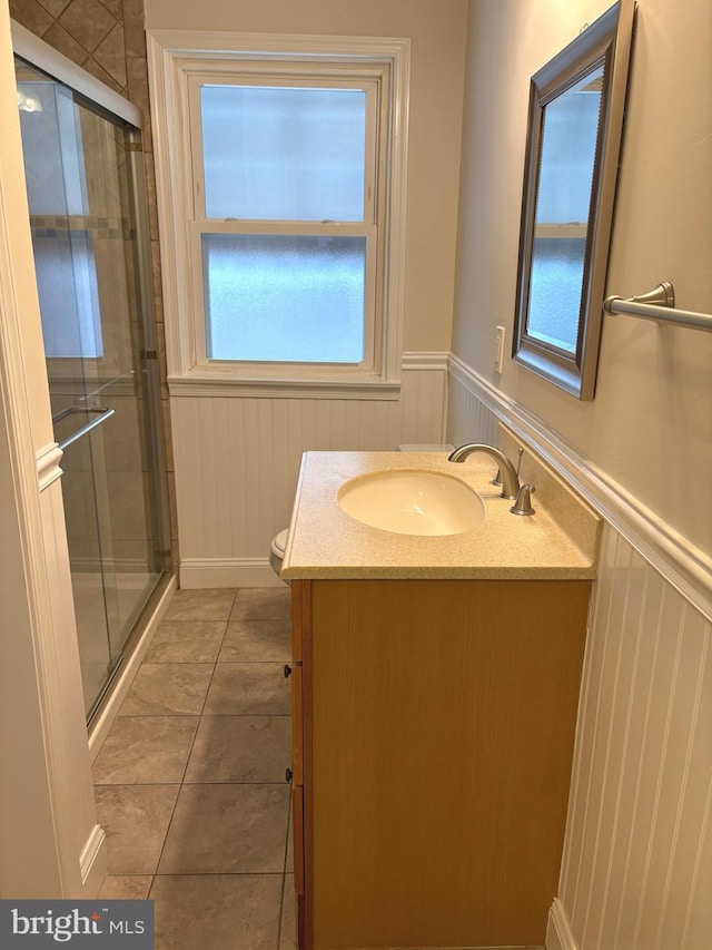 bathroom featuring tile patterned flooring, vanity, toilet, and a shower with shower door