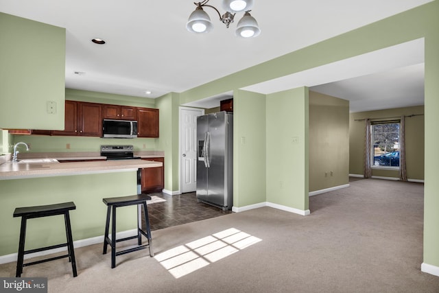 kitchen with appliances with stainless steel finishes, a breakfast bar, sink, dark carpet, and kitchen peninsula