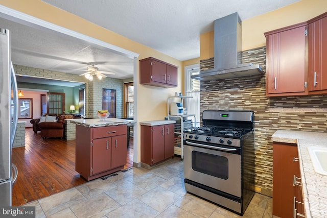 kitchen featuring decorative backsplash, a center island, stainless steel appliances, wall chimney range hood, and a textured ceiling