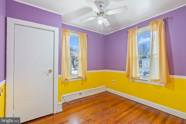 spare room featuring ceiling fan, a healthy amount of sunlight, wood-type flooring, and a baseboard heating unit