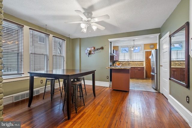 dining area featuring ceiling fan with notable chandelier, dark hardwood / wood-style floors, sink, and a textured ceiling