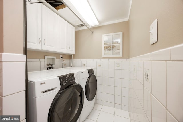 laundry area with independent washer and dryer, cabinets, tile walls, and light tile patterned floors