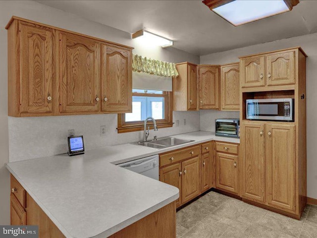 kitchen featuring a peninsula, a sink, light countertops, dishwasher, and stainless steel microwave