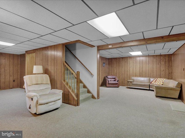 sitting room featuring light carpet, a drop ceiling, stairs, and wooden walls