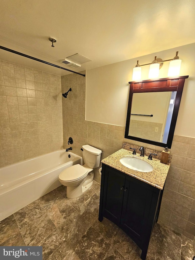 full bathroom featuring toilet, tile walls, vanity, and tiled shower / bath