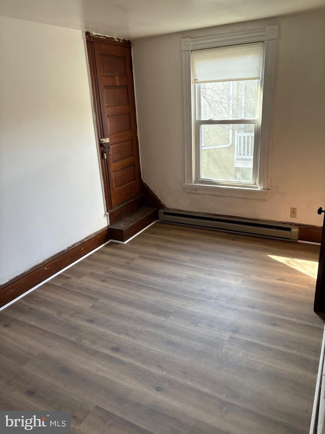 empty room with baseboards, a baseboard heating unit, and wood finished floors