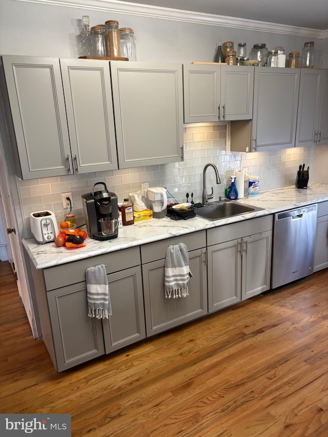 kitchen featuring backsplash, gray cabinets, stainless steel dishwasher, light wood-style floors, and a sink