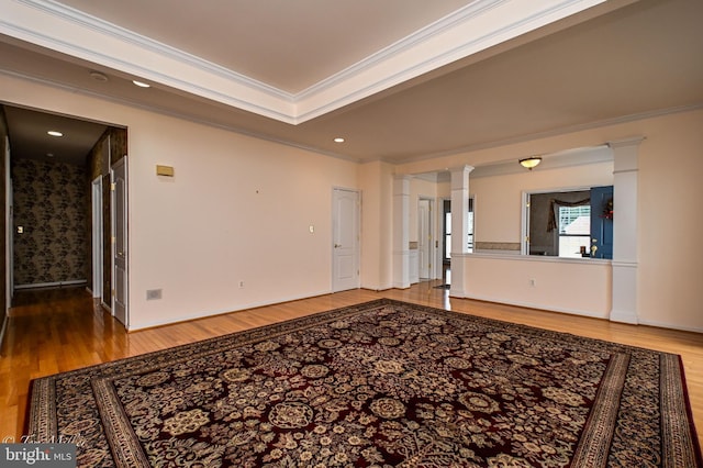 spare room with decorative columns, ornamental molding, a raised ceiling, and wood finished floors