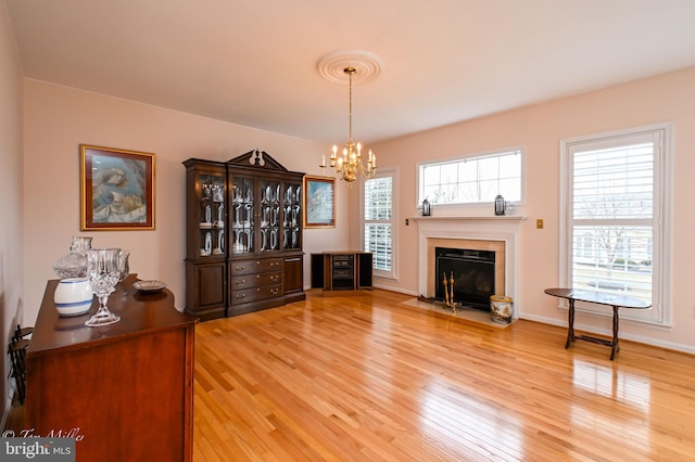 living area with a fireplace with flush hearth, a notable chandelier, baseboards, and wood finished floors