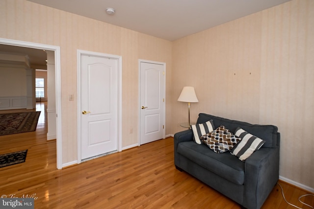 living area featuring wallpapered walls, wood finished floors, and baseboards