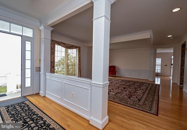 foyer entrance featuring a decorative wall, wood finished floors, ornamental molding, wainscoting, and ornate columns