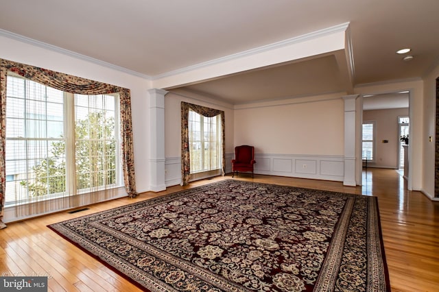 empty room featuring ornate columns, ornamental molding, a wealth of natural light, and a wainscoted wall