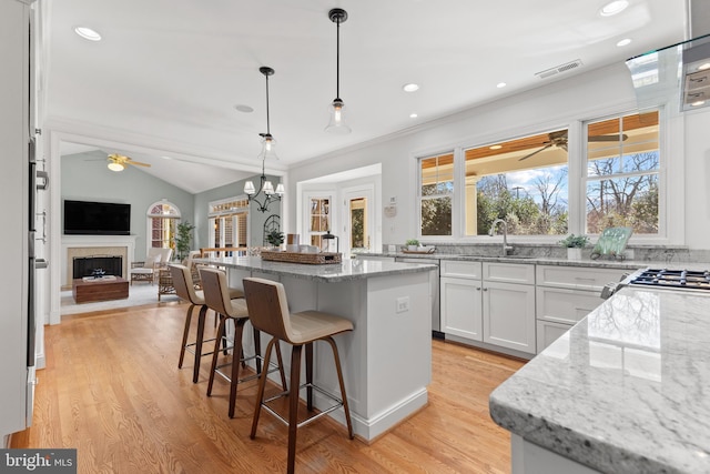 kitchen with white cabinets, hanging light fixtures, light stone counters, and a center island