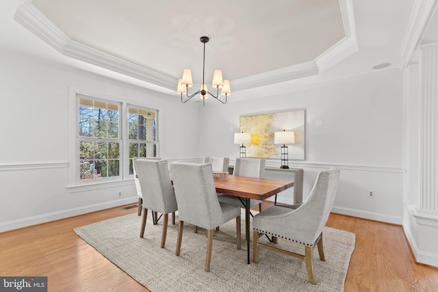 dining area with a notable chandelier, light hardwood / wood-style floors, and a raised ceiling