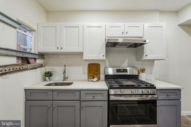 kitchen with gray cabinets, stainless steel gas stove, white cabinetry, sink, and decorative backsplash