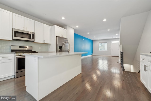 kitchen featuring white cabinetry, dark wood-type flooring, stainless steel appliances, and a center island with sink