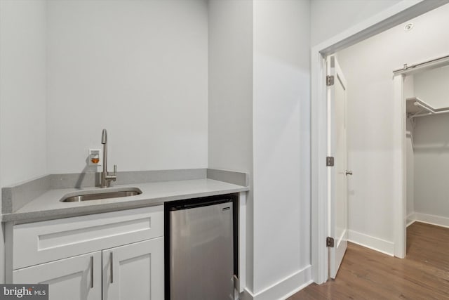 bar with dark hardwood / wood-style flooring, sink, stainless steel fridge, and white cabinets