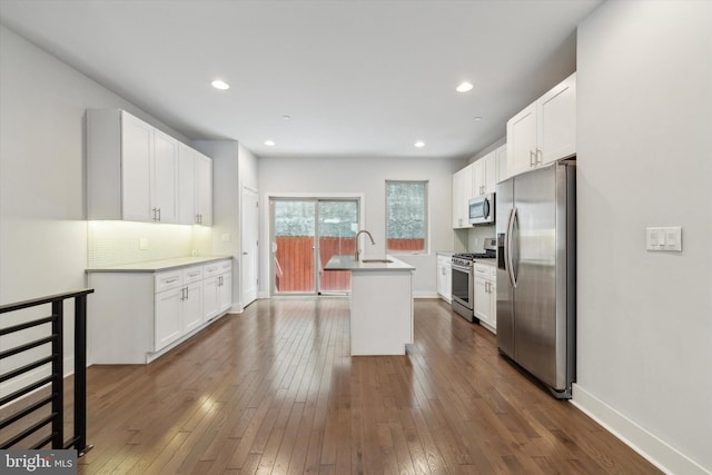 kitchen with white cabinetry, dark hardwood / wood-style floors, stainless steel appliances, a kitchen island with sink, and decorative backsplash