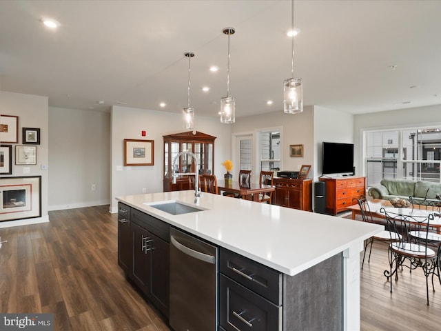 kitchen with decorative light fixtures, sink, dark hardwood / wood-style flooring, stainless steel dishwasher, and a center island with sink