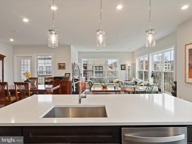 kitchen featuring stainless steel dishwasher, sink, a kitchen island with sink, and hanging light fixtures