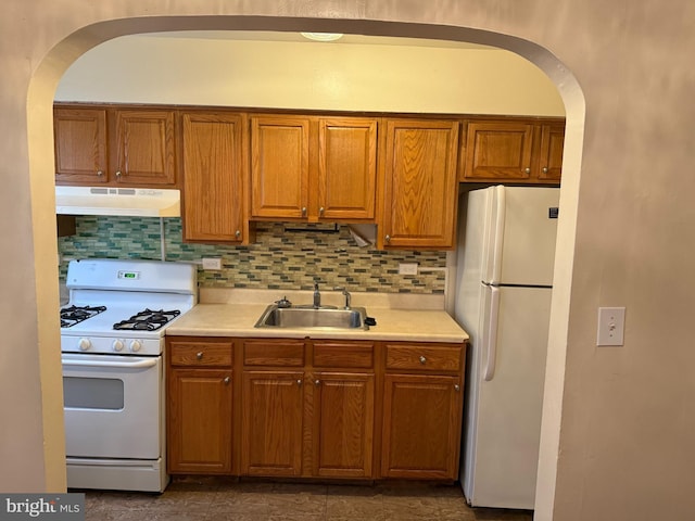 kitchen featuring light countertops, backsplash, a sink, white appliances, and under cabinet range hood