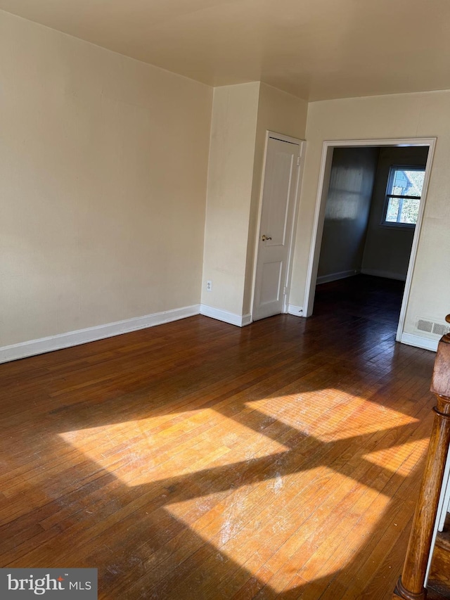 unfurnished room with dark wood-style floors, visible vents, and baseboards