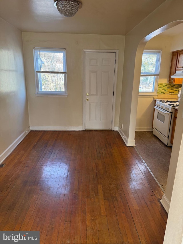 foyer entrance with baseboards, arched walkways, and wood finished floors