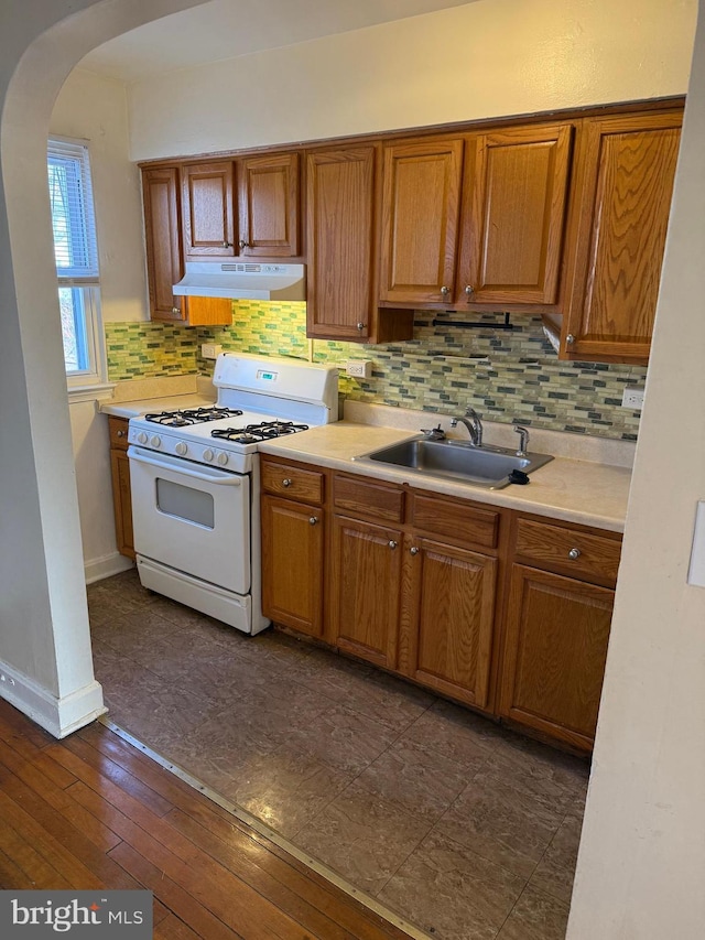 kitchen with arched walkways, under cabinet range hood, a sink, light countertops, and gas range gas stove