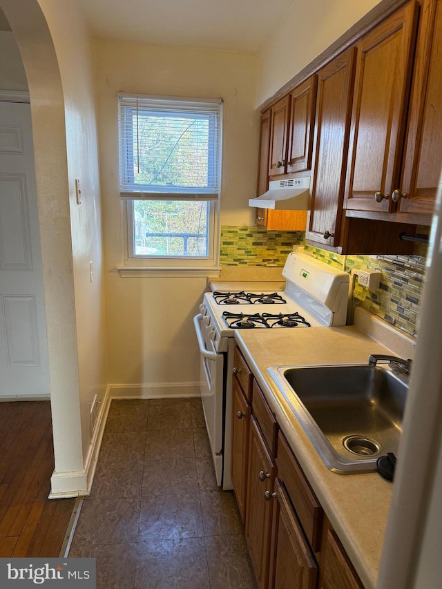 kitchen with light countertops, a sink, under cabinet range hood, and white gas range