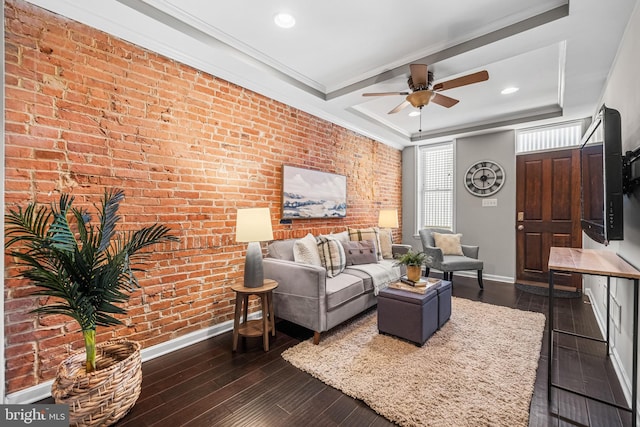 living room featuring brick wall, ceiling fan, a raised ceiling, crown molding, and dark hardwood / wood-style floors