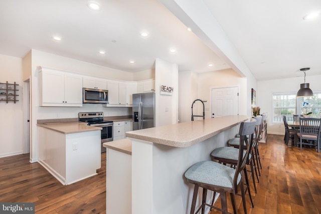 kitchen featuring a breakfast bar area, light countertops, appliances with stainless steel finishes, dark wood-type flooring, and white cabinets