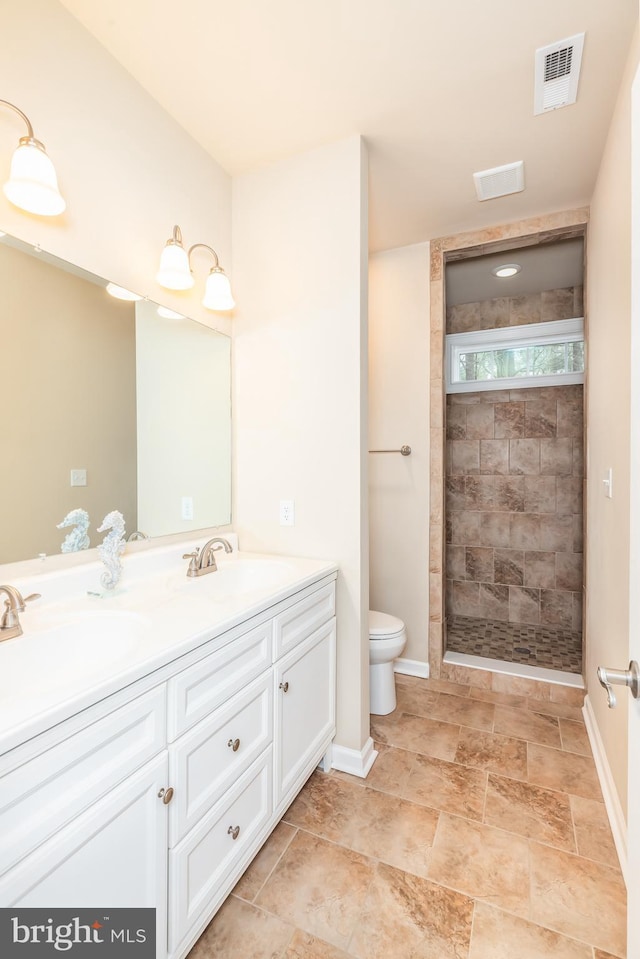 bathroom with toilet, a sink, visible vents, tiled shower, and double vanity