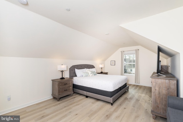 bedroom with light wood-type flooring, baseboards, and vaulted ceiling