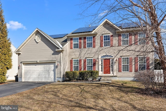 colonial-style house featuring a front yard, roof mounted solar panels, and driveway