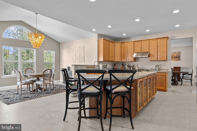 kitchen featuring light stone counters, recessed lighting, an inviting chandelier, under cabinet range hood, and a kitchen breakfast bar