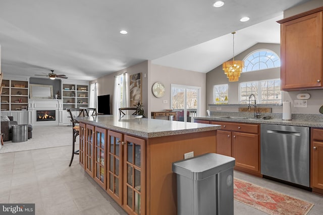 kitchen featuring a sink, a lit fireplace, brown cabinetry, and stainless steel dishwasher