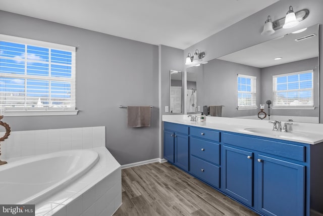 bathroom featuring a garden tub, double vanity, visible vents, a sink, and wood finished floors