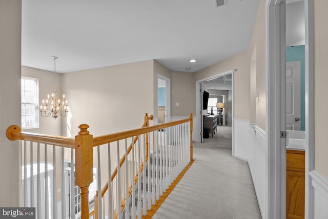 hall with a wainscoted wall, a notable chandelier, recessed lighting, light carpet, and an upstairs landing