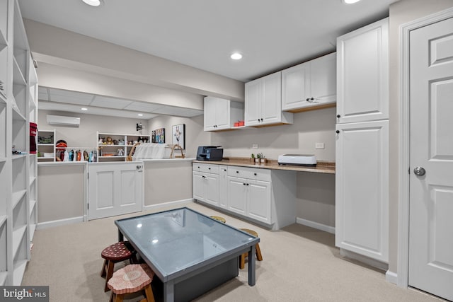 kitchen featuring light carpet, a wall unit AC, white cabinetry, built in desk, and recessed lighting