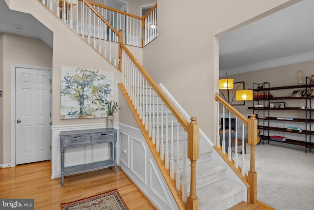 stairway with ornamental molding, wood finished floors, and a towering ceiling