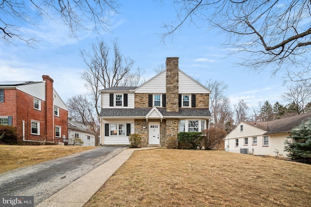 view of front facade featuring a front yard, stone siding, driveway, and a chimney