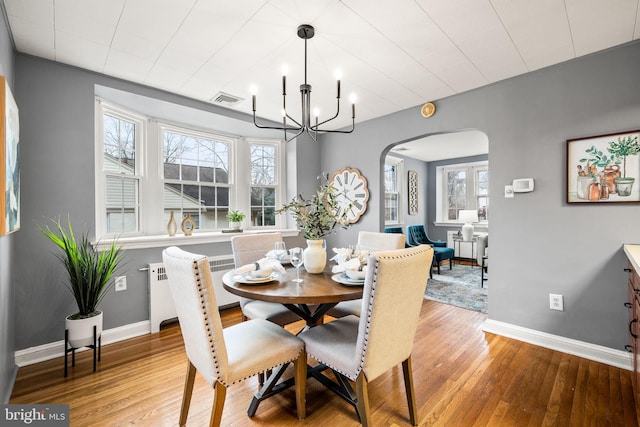 dining area featuring arched walkways, wood-type flooring, visible vents, and an inviting chandelier