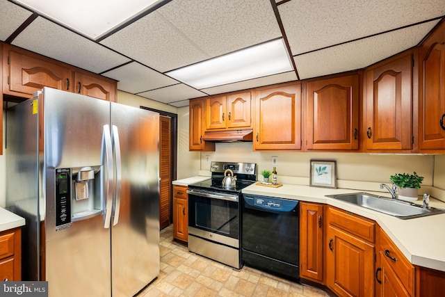 kitchen with appliances with stainless steel finishes, light countertops, a paneled ceiling, under cabinet range hood, and a sink