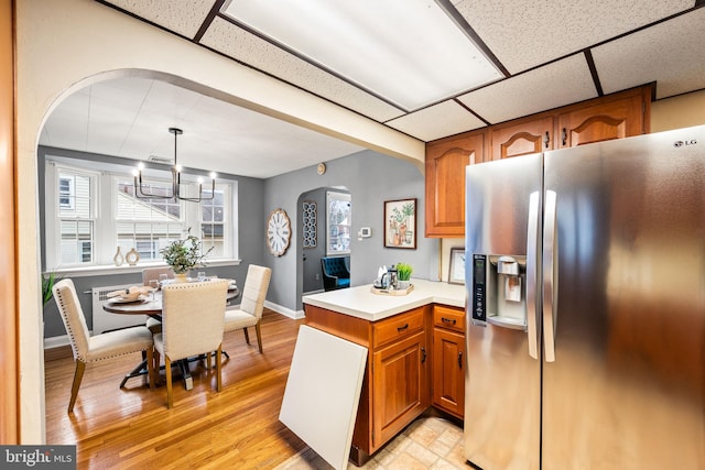 kitchen with arched walkways, brown cabinetry, a drop ceiling, and stainless steel fridge