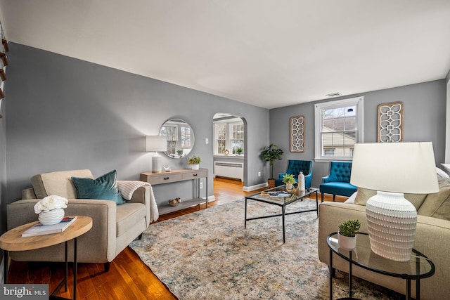 living room with arched walkways, wood finished floors, visible vents, and baseboards